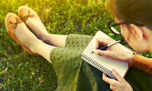 Girl,With,Pen,Writing,On,Notebook,On,Grass,Outside